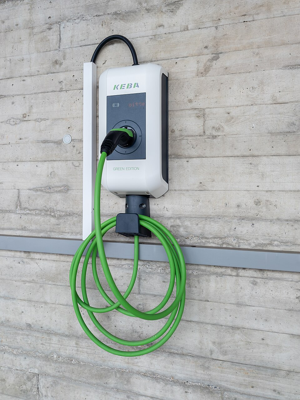 Väggmonterad elbilsladdare KEBA KeContact P30 med grön kabel ansluten, GREEN EDITION, på en betongvägg